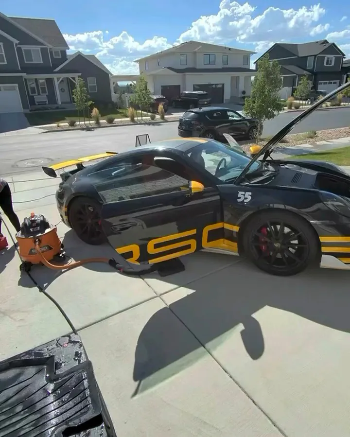 Black and yellow Porsche being detailed in a driveway with professional equipment