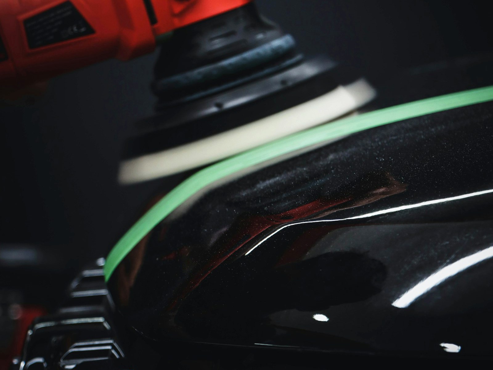 Dual-action polisher buffing a glossy black car panel during paint correction