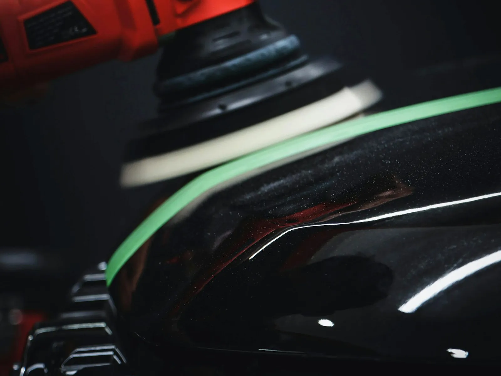 Dual-action polisher buffing a glossy black car panel during paint correction